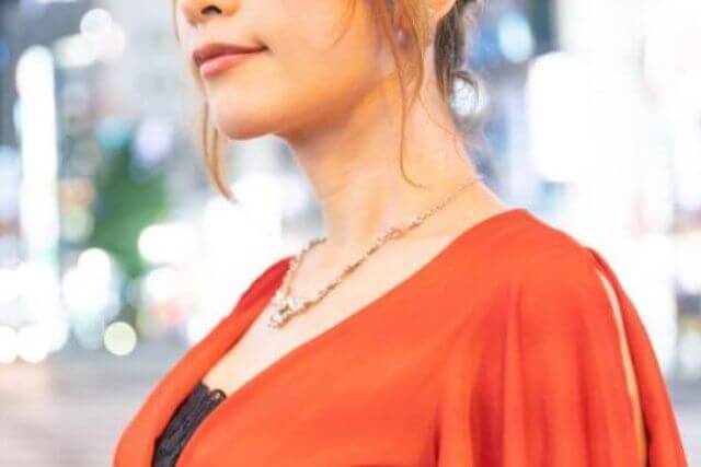 繁華街に立つオレンジの服を着た女性の口元