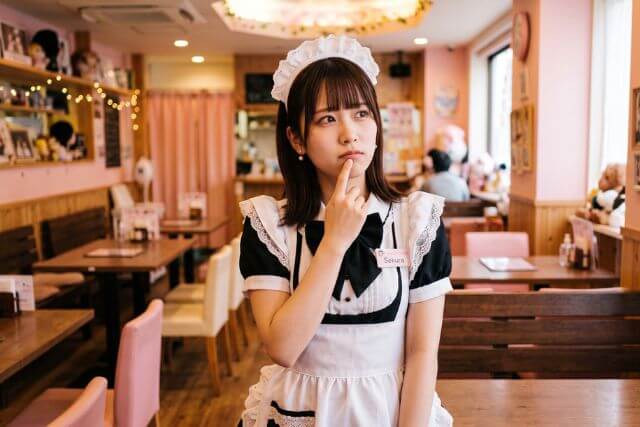 メイド喫茶で口に手を当てて悩む表情のメイドの女性