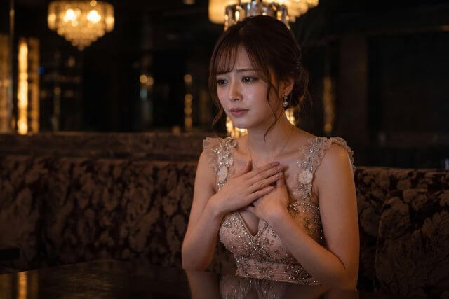 胸を押さえて座っているドレスの女性