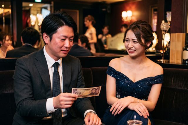 5000円札を持っているスーツの男性と苦笑いするドレスの女性