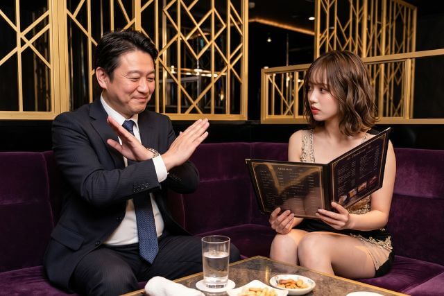 笑顔で手をクロスする男性とメニューを見せるドレスの女性