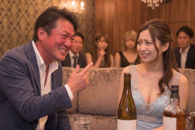 赤ら顔で笑顔で話すスーツの男性と苦笑いのキャバ嬢