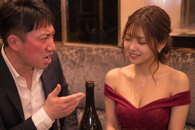 怒った表情のスーツの男性といなすような笑顔のキャバ嬢
