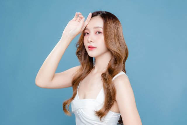 水色の壁の前で頭に手を当てているロングヘアの女性