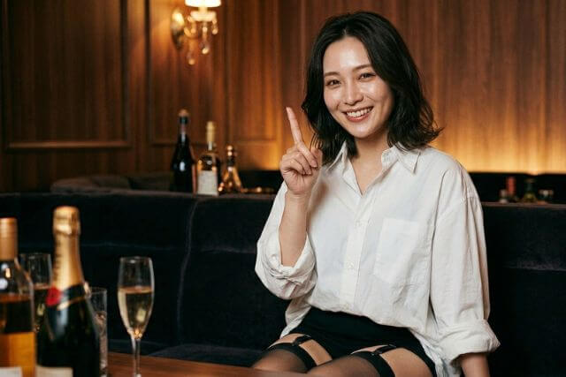 ワイシャツを着た女性が人差し指を立てて笑顔で座っている