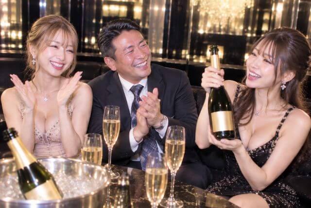 ワインボトルを持つ黒いドレスの女性と手拍子するドレスの女性とスーツの男性