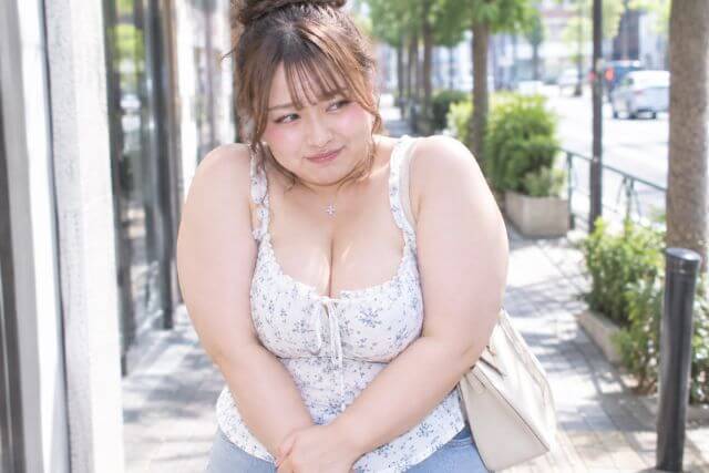 白いキャミソールを着て恥ずかしそうに歩道に立つふくよかな女性