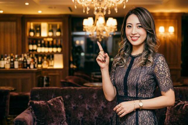 キャバクラ店内で人差し指を立てて立っているキャバ嬢の女性