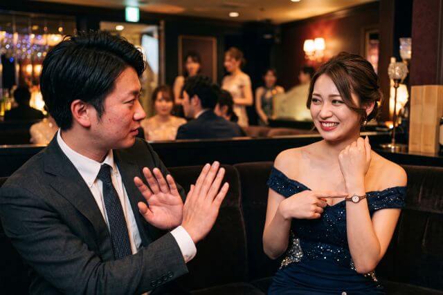 時計を指差すドレスの女性と手をクロスするスーツの男性
