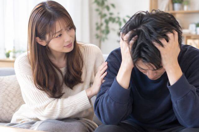 頭を抱えている男性に対して優しい笑顔で話しかける女性