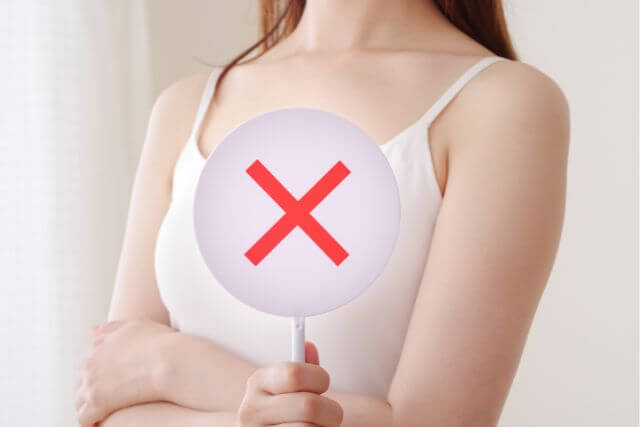 バツ印が書かれた札を持つ女性の上半身