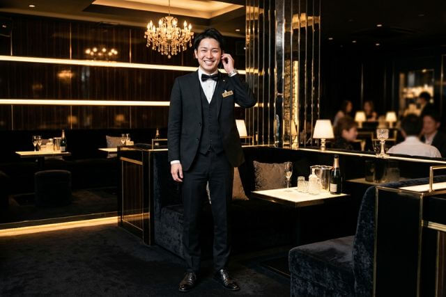 キャバクラ店内で耳に手を当てる黒服の男性