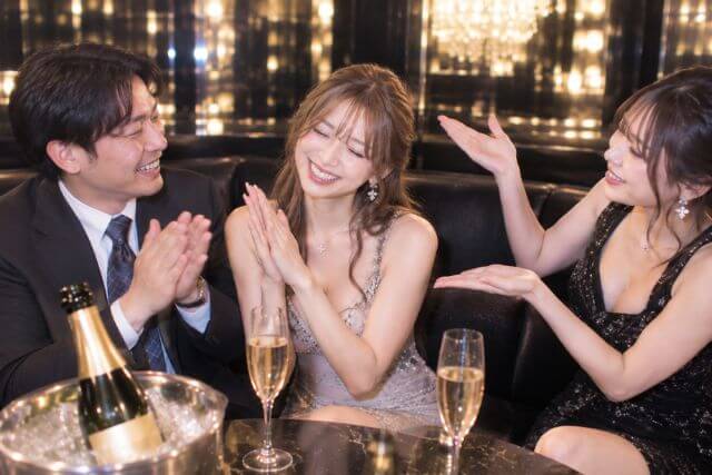 手拍子するドレスの女性とスーツの男性の横で、手を広げている女性