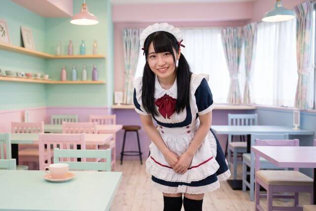 パステルカラーの店内でメイド服を着てお辞儀する女性
