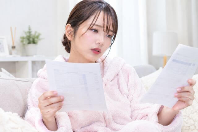 2枚の紙をみている部屋着の女性