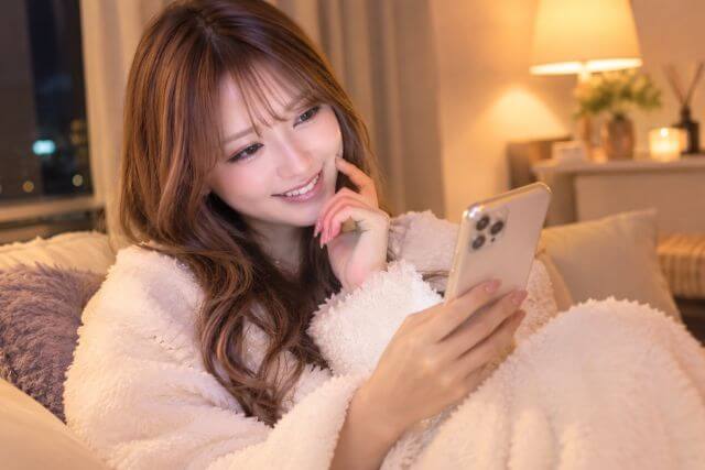 部屋着を着てスマホを見て微笑む女性