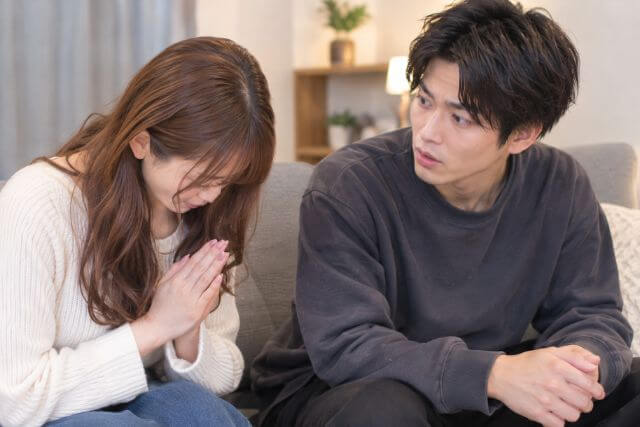 ソファに横並びに男女が座っていて、女性が男性に対して謝罪をしている様子