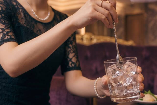 氷が入ったグラスにマドラーを刺す女性の手元
