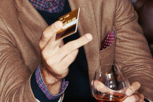 グラスを持ちながら右手でクレジットカードを差し出す男性