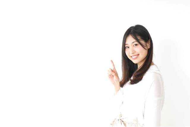 白い服を着て人差し指を立てる若いロングヘアの女性