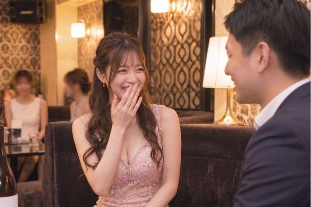 スーツの男性と話す笑顔のキャバ嬢。口に手を当てている