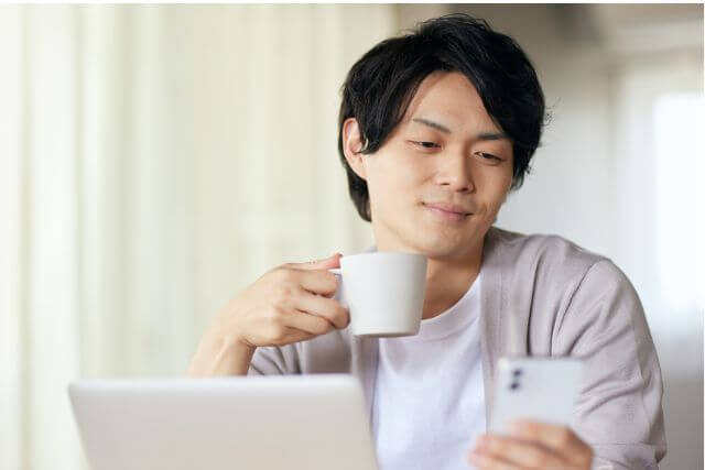 マグカップを持って反対の手でスマホを持っている男性