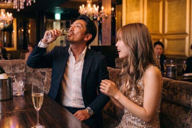 シャンパンを一気飲みするスーツの男性とドレスの女性