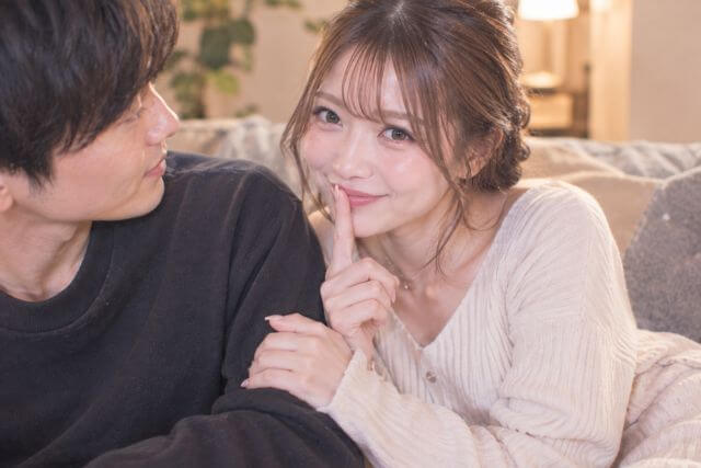 ソファで男性の腕にもたれかかって人差し指を口に当てて笑顔の女性