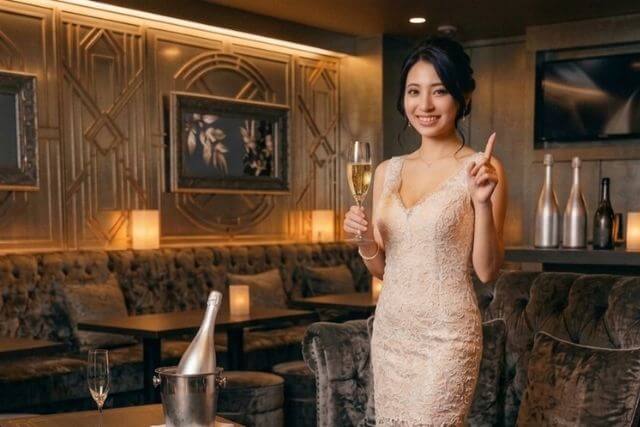 キャバクラ店内でグラスを持ちながら人差し指を立てるキャバ嬢