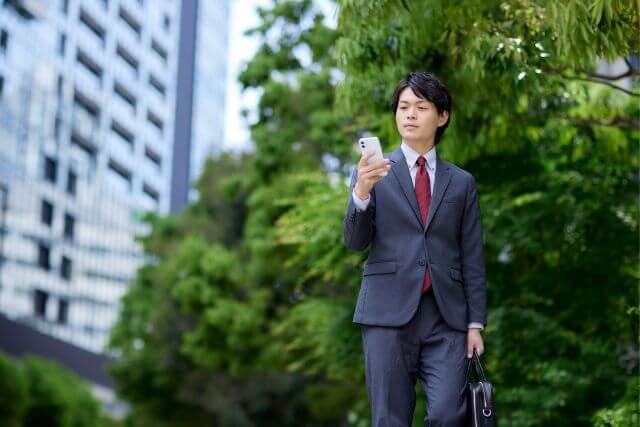 スーツで屋外を歩くスマホを持った男性