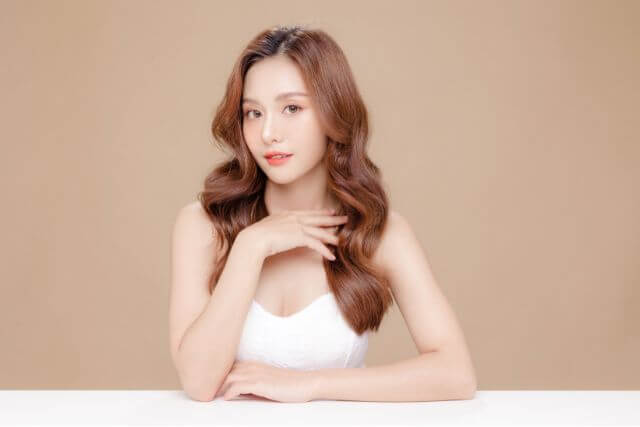 茶髪のロングヘアの女性がテーブルに手をついて座っている
