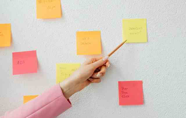 壁に貼られたカラフルな付箋とペンで指さす手