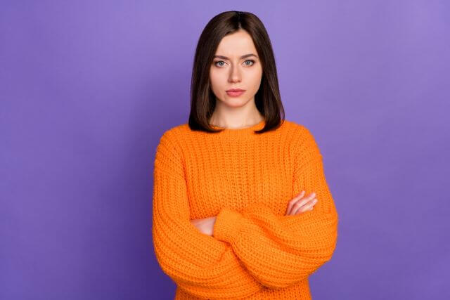 腕を組んでいるオレンジの洋服を着た女性