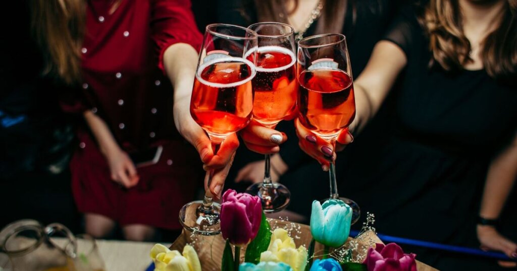 赤いシャンパンが入ったグラスを持つ3人の女性の手