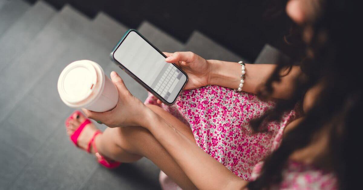 階段で携帯とコーヒーを持つ女性