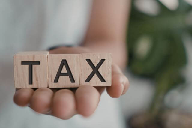 Taxと書かれた木のブロックを持つ手