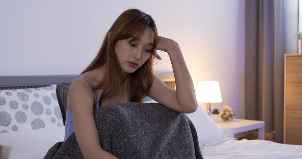 ベッドの上で悲しそうに俯くロングヘアの女性