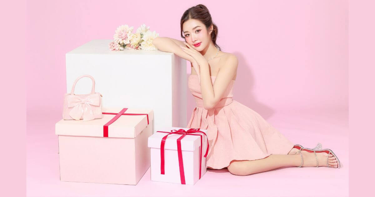 ピンクの部屋でプレゼントボックスに寄りかかるピンクのドレスを着た若い女性