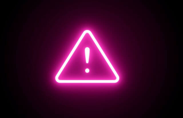 黒い背景にあるピンクのネオンの注意マーク
